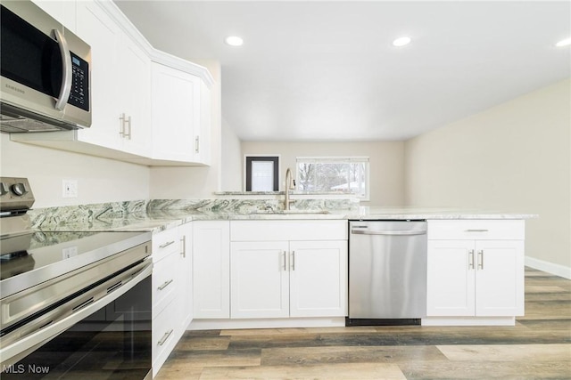 kitchen with light stone countertops, white cabinetry, sink, stainless steel appliances, and light hardwood / wood-style floors