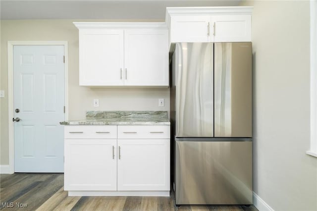 kitchen featuring hardwood / wood-style floors, light stone counters, white cabinetry, and stainless steel refrigerator