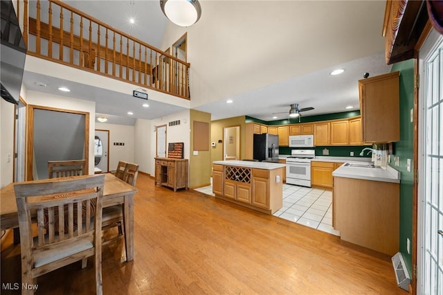 kitchen with white appliances, ceiling fan, light countertops, light wood finished floors, and a towering ceiling