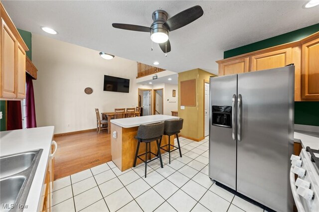 kitchen with stainless steel fridge with ice dispenser, a sink, ceiling fan, a breakfast bar, and a center island