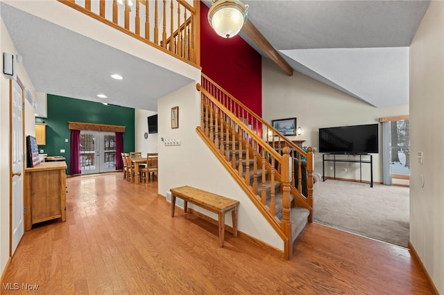 stairway with beamed ceiling, hardwood / wood-style floors, high vaulted ceiling, and french doors