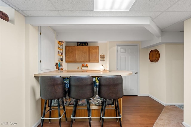 kitchen with kitchen peninsula, a kitchen breakfast bar, a drop ceiling, and hardwood / wood-style floors