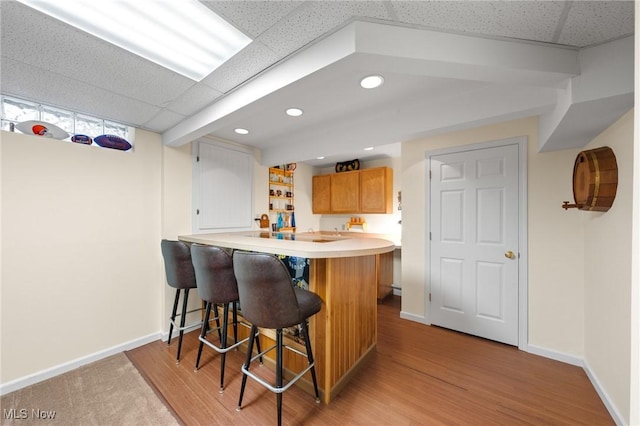 kitchen with baseboards, a kitchen breakfast bar, light countertops, a peninsula, and light wood-style flooring