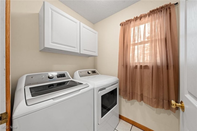 washroom featuring washing machine and dryer, light tile patterned floors, cabinets, and a textured ceiling