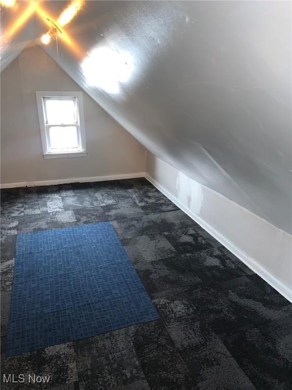 bonus room with dark carpet and vaulted ceiling