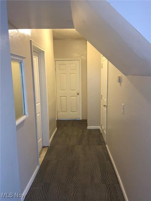 hall with vaulted ceiling and dark colored carpet