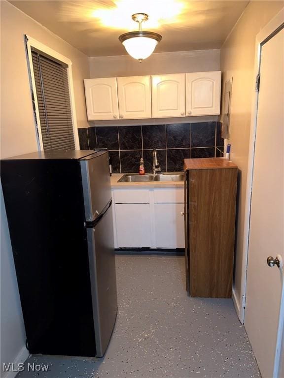 kitchen featuring tasteful backsplash, white cabinetry, sink, and fridge