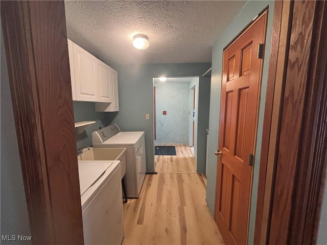 washroom featuring cabinets, light wood-type flooring, washing machine and dryer, and a textured ceiling