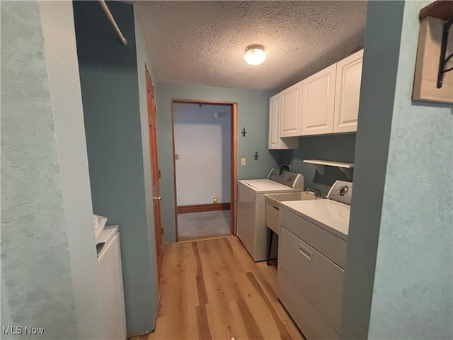 clothes washing area with cabinets, a textured ceiling, light wood-type flooring, and washer and clothes dryer