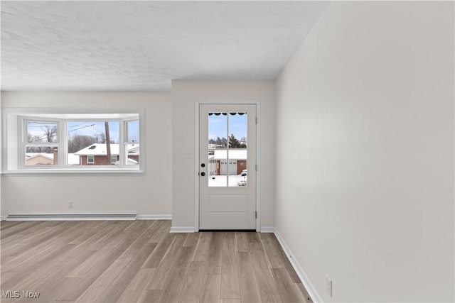 doorway to outside featuring a textured ceiling, light hardwood / wood-style flooring, and a baseboard heating unit