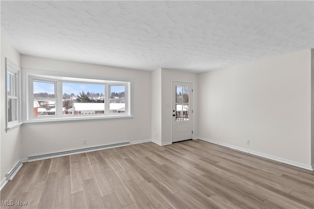 unfurnished room with a textured ceiling, light wood-type flooring, and a baseboard heating unit