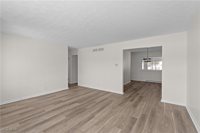 unfurnished room with light wood-type flooring, a baseboard radiator, and a notable chandelier