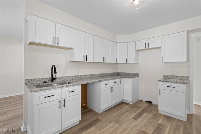 kitchen with light stone countertops, sink, white cabinets, and light wood-type flooring