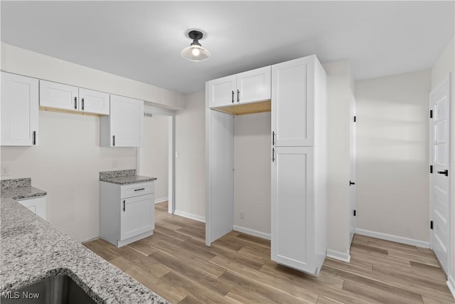 kitchen featuring white cabinets, light wood-type flooring, and light stone counters