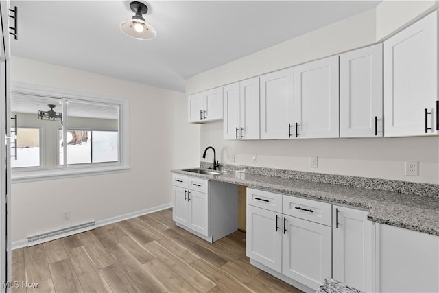 kitchen featuring white cabinets, light stone counters, sink, and light hardwood / wood-style flooring