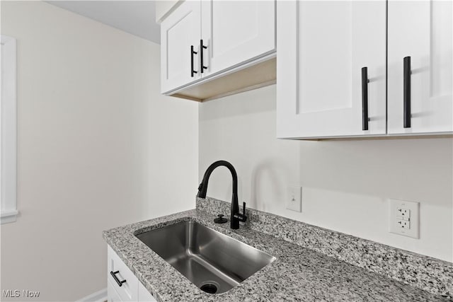 kitchen with white cabinets, light stone counters, and sink