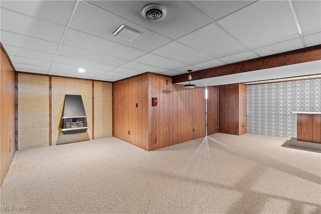 basement with carpet flooring, a drop ceiling, and wood walls