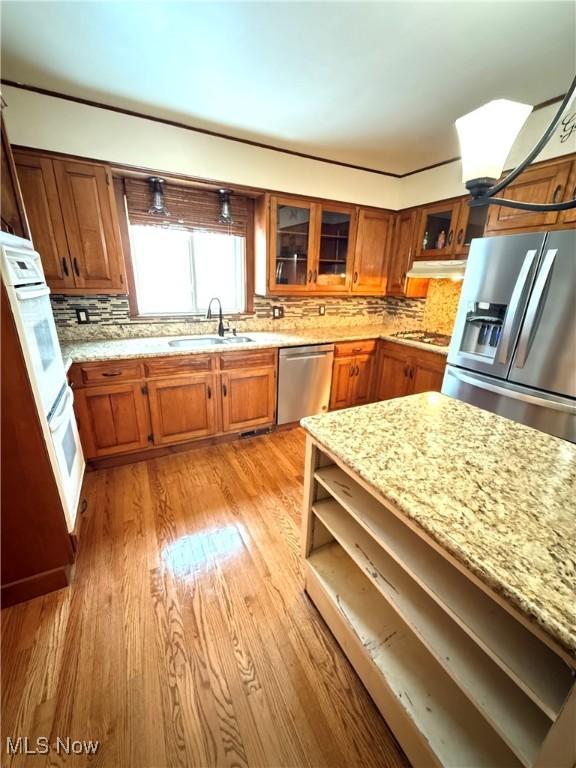 kitchen featuring sink, light hardwood / wood-style flooring, tasteful backsplash, light stone counters, and stainless steel appliances