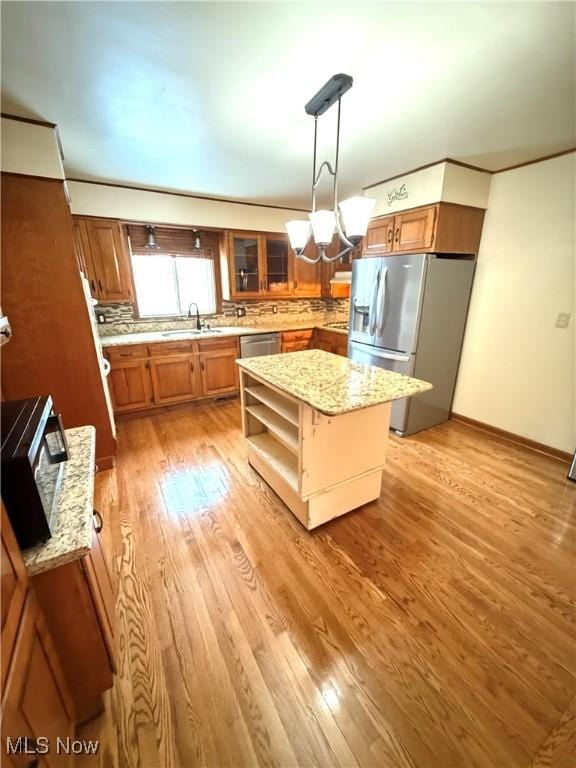 kitchen featuring a center island, decorative backsplash, light wood-type flooring, appliances with stainless steel finishes, and decorative light fixtures