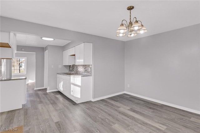 kitchen with decorative backsplash, sink, a notable chandelier, white cabinets, and light hardwood / wood-style floors