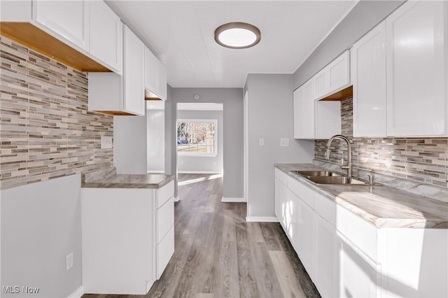 kitchen featuring white cabinets, light wood-type flooring, sink, and tasteful backsplash