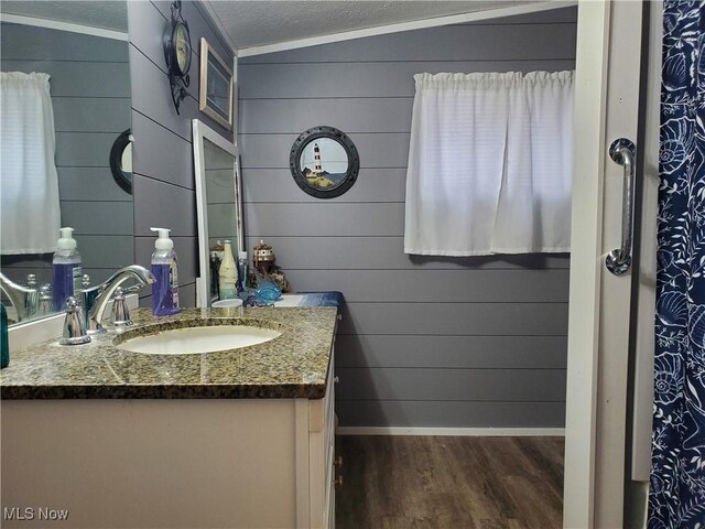 bathroom with wooden walls, hardwood / wood-style floors, lofted ceiling, crown molding, and vanity