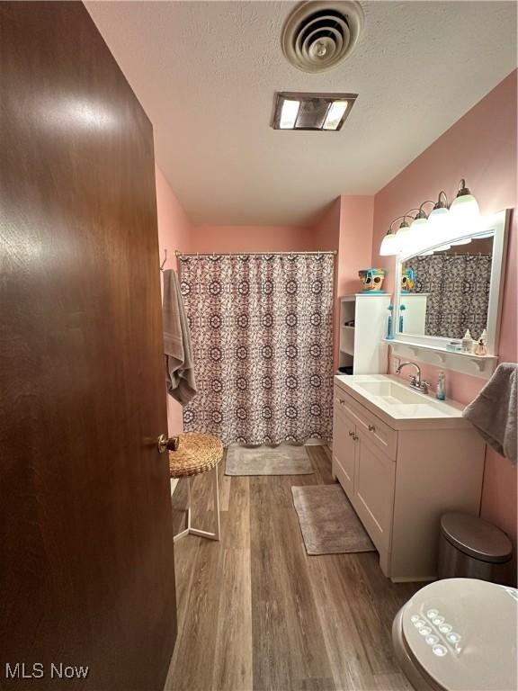 bathroom featuring wood-type flooring, vanity, a textured ceiling, and toilet