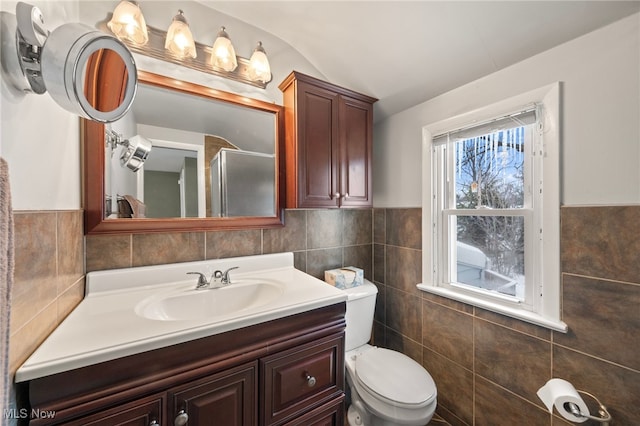 bathroom featuring vanity, vaulted ceiling, toilet, tile walls, and a shower with shower door