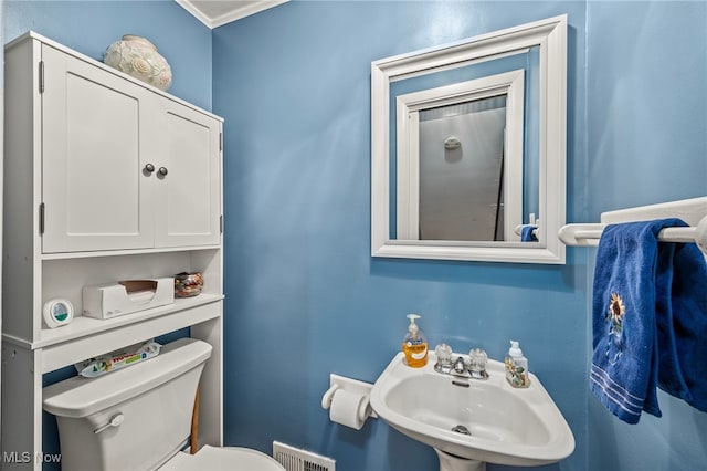 bathroom featuring toilet, crown molding, and sink