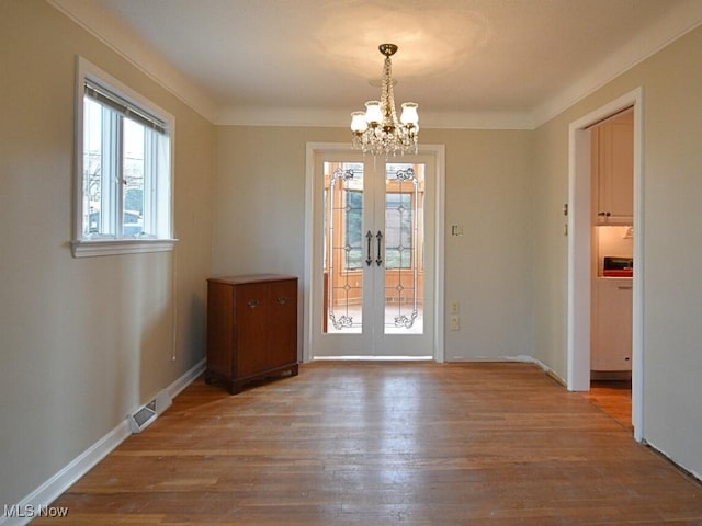 unfurnished dining area featuring french doors, an inviting chandelier, crown molding, and wood-type flooring