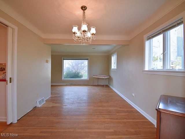 unfurnished dining area featuring wood-type flooring, an inviting chandelier, ornamental molding, and a healthy amount of sunlight