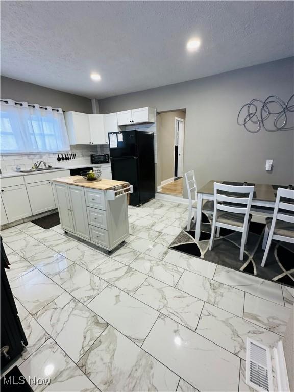 kitchen featuring black refrigerator, white cabinets, a textured ceiling, and wood counters