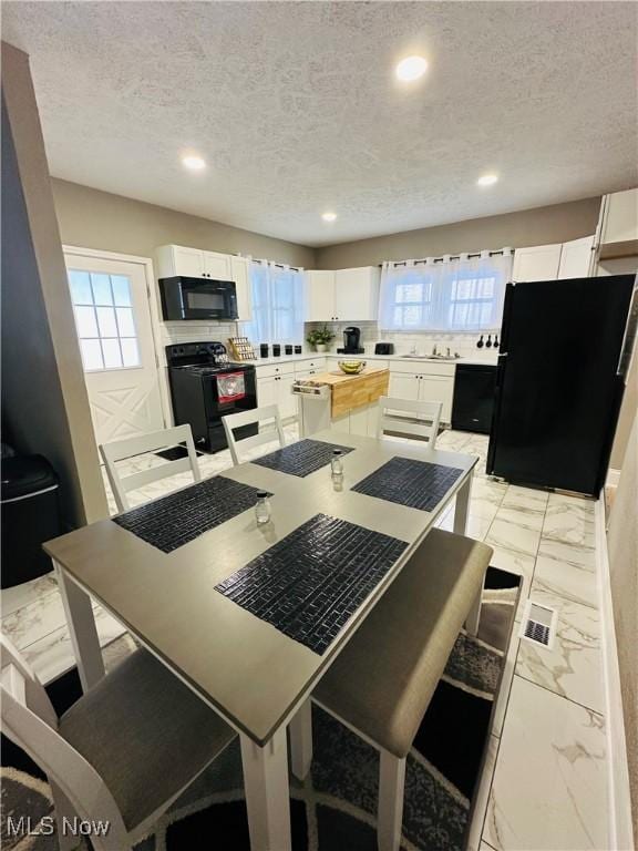 kitchen with black appliances, a center island, white cabinets, and a textured ceiling