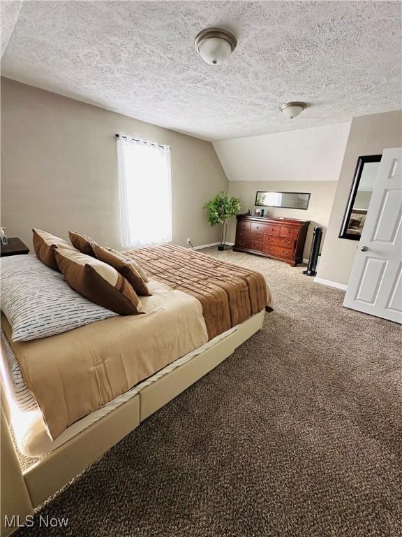 carpeted bedroom featuring a textured ceiling and vaulted ceiling