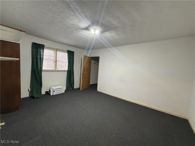 unfurnished bedroom featuring a wall mounted AC, a textured ceiling, and dark colored carpet