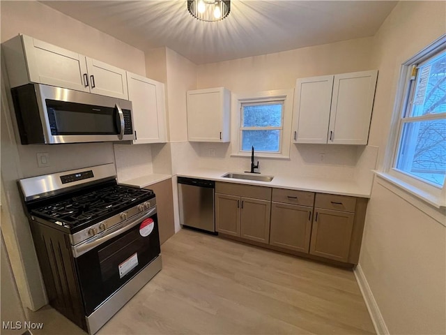 kitchen with appliances with stainless steel finishes, light wood-type flooring, a wealth of natural light, sink, and white cabinets