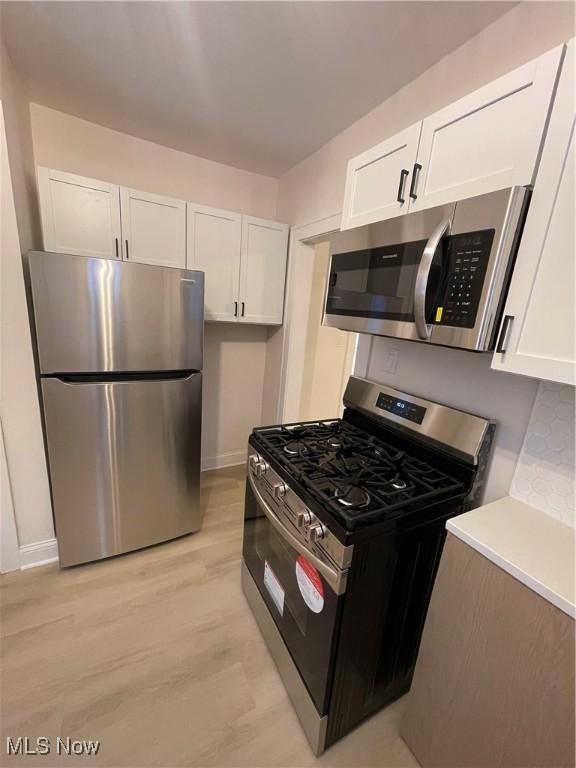 kitchen with light hardwood / wood-style flooring, white cabinets, and stainless steel appliances