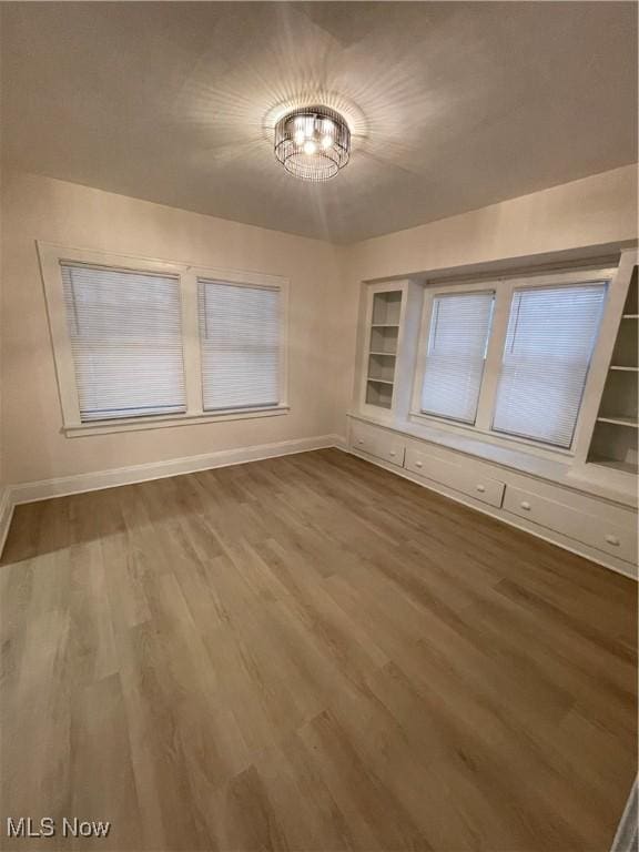 unfurnished room featuring a chandelier, built in shelves, and wood-type flooring