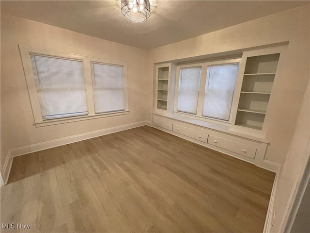 unfurnished dining area featuring hardwood / wood-style flooring, built in shelves, and an inviting chandelier