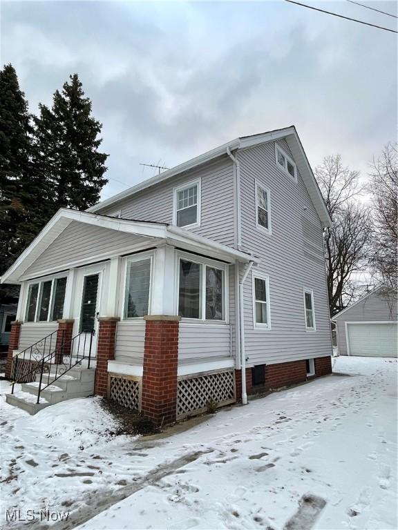 snow covered rear of property featuring an outdoor structure and a garage