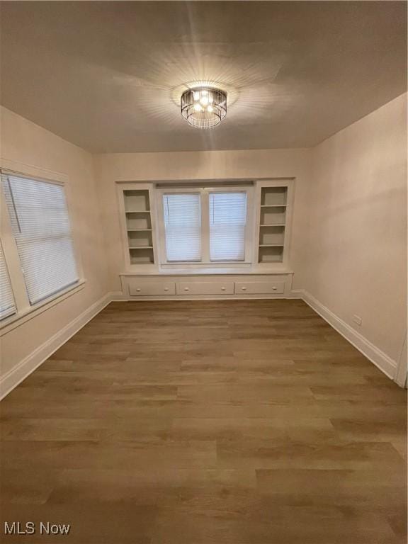 unfurnished room featuring hardwood / wood-style flooring, built in shelves, and an inviting chandelier