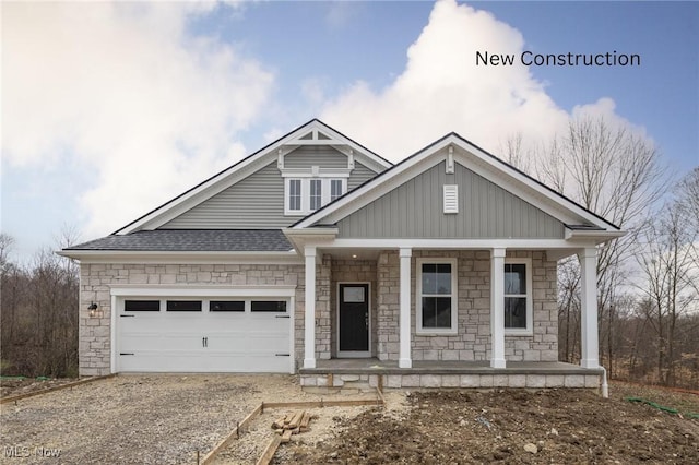 craftsman inspired home with a porch, roof with shingles, stone siding, gravel driveway, and a garage