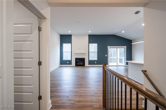 unfurnished living room with a healthy amount of sunlight, a large fireplace, vaulted ceiling, and wood finished floors