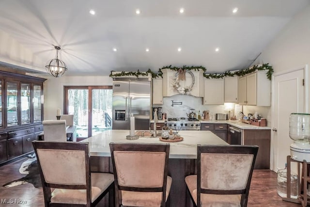 kitchen featuring hanging light fixtures, light stone counters, premium range hood, a center island with sink, and high end appliances