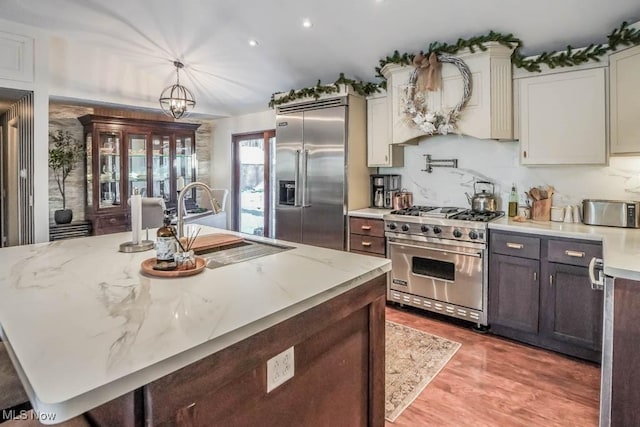 kitchen with pendant lighting, sink, light stone countertops, premium appliances, and a chandelier