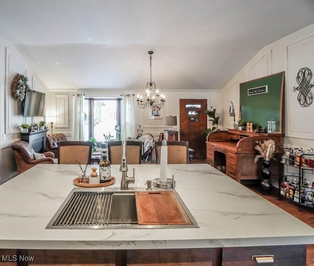 kitchen with light stone countertops, sink, a chandelier, pendant lighting, and lofted ceiling