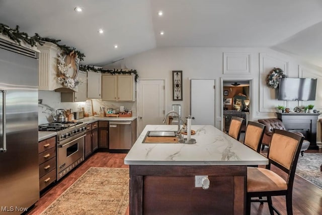 kitchen with backsplash, vaulted ceiling, sink, a center island with sink, and high quality appliances