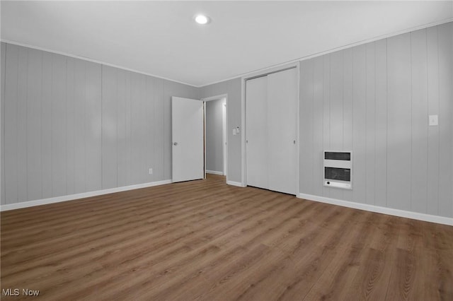 unfurnished bedroom with a closet, wood-type flooring, ornamental molding, and heating unit