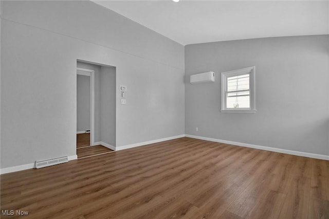 spare room featuring an AC wall unit, hardwood / wood-style floors, and vaulted ceiling