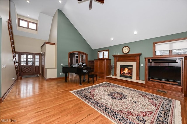 living room with a high end fireplace, high vaulted ceiling, light hardwood / wood-style floors, and ceiling fan